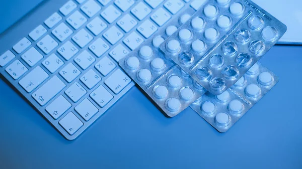 Keyboard and blistered pills on blue background. Work and health concept