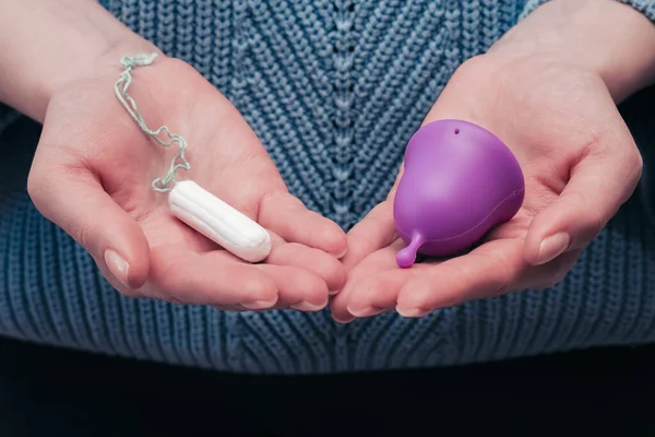 Adet bardağı ve tampon tutan kadın elleri. Regl hijyen ürünleri karşılaştırması. Kadın hijyeni ve sağlık konsepti