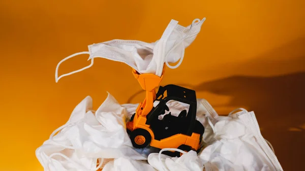 Kullanılmış tıbbi maske takan oyuncak traktör. Tıbbi atık ve kirlilik kavramı