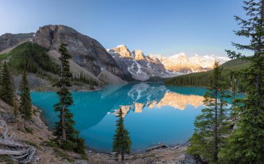 Panoramic view of beautiful sunrise over turquoise waters of the Moraine Lake with snow-covered peaks above it in Rocky Mountains, Banff National Park, Canada.	