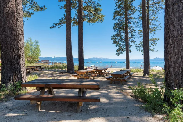 Wooden tables and benches in picnic area near Lake Tahoe beach with  and pine trees, California