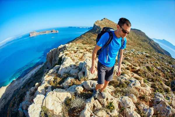Deniz ve mavi gökyüzü karşı Uçurumdaki erkek seyahat sırt çantası ile çalışır — Stok fotoğraf