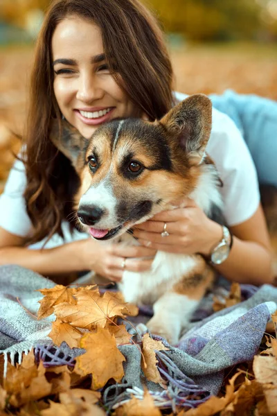 在秋天的公园里，一个快乐的女人和她的爱犬威尔士科尔吉。背景上的桔黄色落叶. — 图库照片
