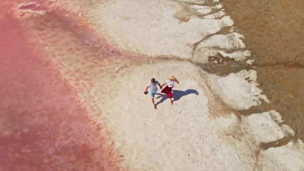 Pasangan muda yang indah berjalan di sepanjang danau merah muda yang indah dengan pantai asin — Stok Video