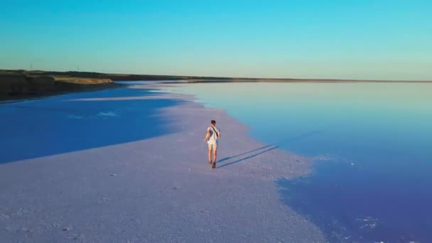 Вид ззаду на повітря молодий чоловік, що біжить на сухому соляному пляжі — стокове відео