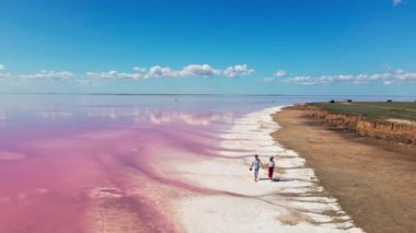 Pembe mineral gölünün kıyısında yürüyen sevimli bir çiftin hava görüntüleri.