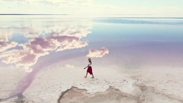 Kırmızı etekli mutlu kaygısız kadın bulutların yansımasıyla tuzlu göl kıyısında yürüyor. — Stok video
