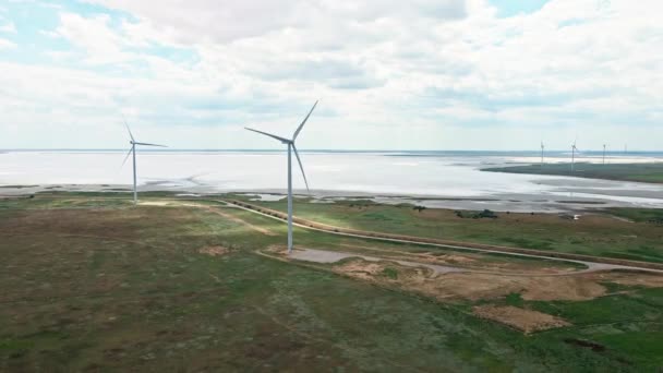 Drone voando em linha reta na turbina eólica céu nublado e lago no fundo — Vídeo de Stock