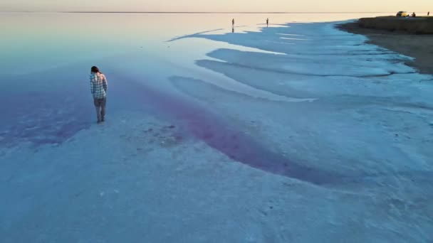 ドローンビュー若い女性はミネラル塩湖の塩の海岸に沿って歩く — ストック動画