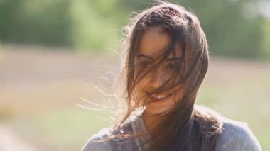 Sakin, güzel, gülen bir kadın. Güneşli bir sonbahar gününde saçlarını savuruyor.