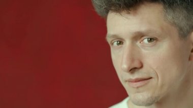 Bir erkek kırmızı arka plana bakarak birine göz kırpar.