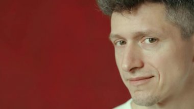 Bir erkek kırmızı arka plana bakarak birine göz kırpar.