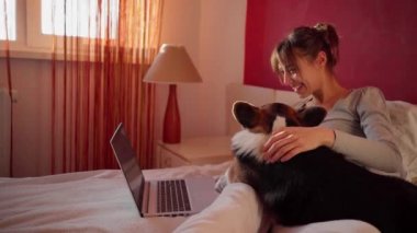 Mutlu bir kadın evde yatıp erkek arkadaşıyla sohbet ediyor. Laptop bilgisayarında video görüşmesi yapıyor. Kablosuz internet kullanıyor..
