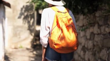 Kamera, kot şortlu, hasır şapkalı ve beyaz gömlekli güzel seksi kızı takip ediyor. Dar yolda merdivenlerden yukarı çıkıyor.