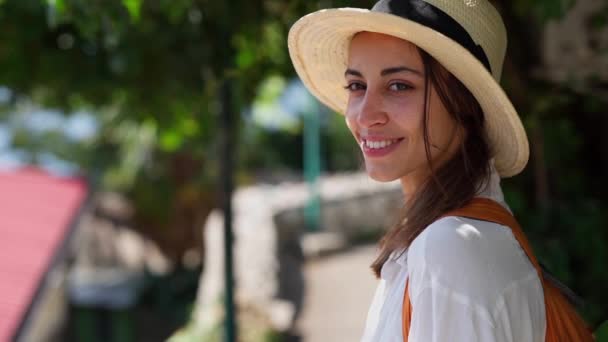 Обличчя впевненої радісної жінки мандрівника в солом'яному капелюсі, що стоїть на зеленій вулиці міста — стокове відео