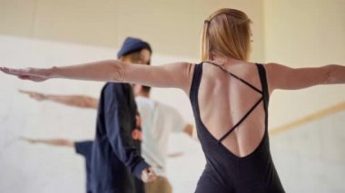 Grup yoga dersinde koçla birlikte, Warrior pozu vererek yoga yapıyor.