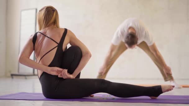 Back view s of sporty flexible woman in black sportswear practicing yoga in yoga class, making stretching back on mat. — Stock Video