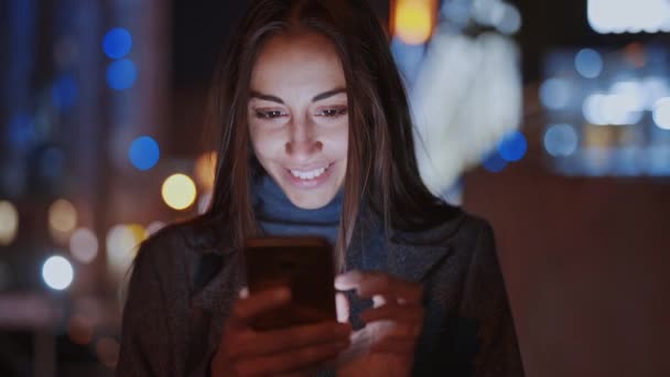 Close-up van de prooi lachende vrouw met behulp van smartphone lopen 's nachts stad — Stockvideo