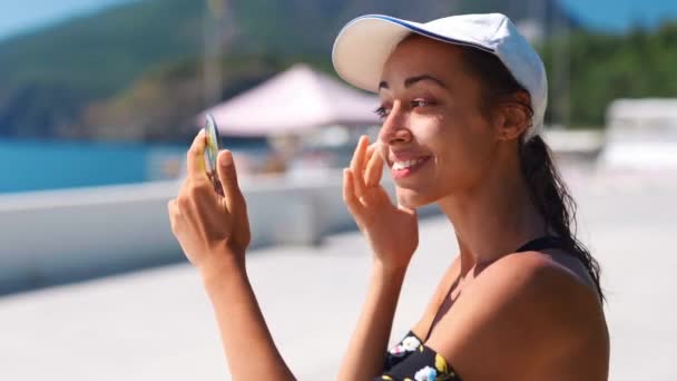 Mujer en el soleado día de verano mirando el espejo y pone crema solar en la cara — Vídeos de Stock