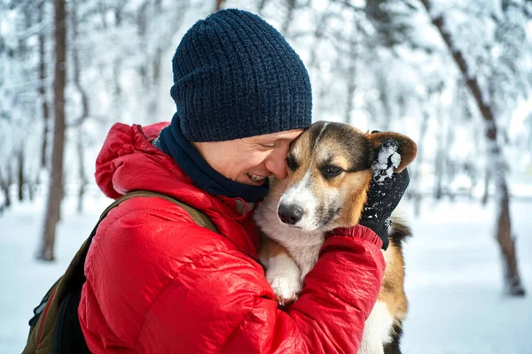 Portrait pleased man embracing dog Welsh Corgi with eyes closed outdoors in winter landscape — Stock Photo, Image