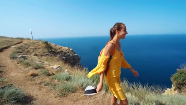 Kvinna gul solklänning njuter av utsikt över stranden och bukten promenader på branta kusten — Stockvideo