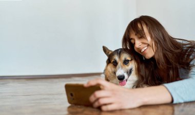 Çekici gülüşü olan bir kadın oturma odasında evcil hayvanıyla uzanıyor ve selfie çekiyor..