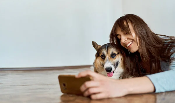 Femeie cu zâmbet fermecător întinsă pe podea în camera de zi cu animale de companie și făcând fotografie selfie . — Fotografie, imagine de stoc