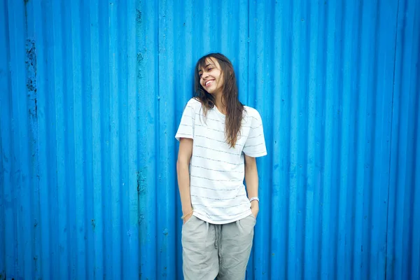 Young latin woman standing by bright blue wall, looking to side with smile Stock Image