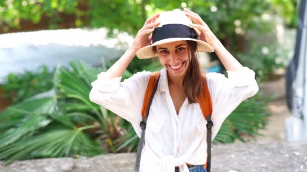Красива радісна туристична жінка в солом'яному капелюсі і білій сорочці дивиться і посміхається на камеру — стокове відео