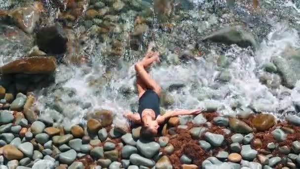 Top view vacker smal flicka i svart baddräkt ligger på stenstrand i vatten — Stockvideo