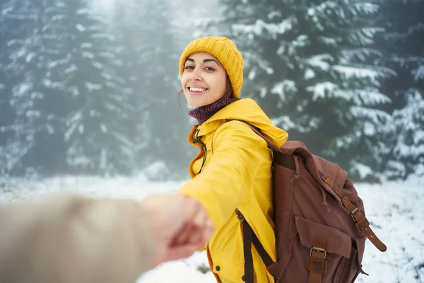 Wanita optimis dengan pakaian hangat kuning cerah dengan tas punggung memegang tangan seseorang, ikut saya ke hutan berkabut musim dingin — Stok Foto