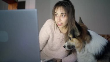 Kanepede köpeğiyle oturan kadın dizüstü bilgisayarında bir şey gösteriyor.