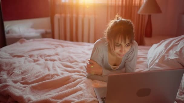 Giovane donna sdraiata sul letto a casa e guardando il computer portatile, navigando su Internet. — Video Stock