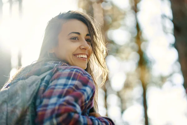 Gros plan portrait extérieur femme souriante dans la forêt avec des rayons de soleil sur l'arrière-plan, exprimant une émotion positive. — Photo