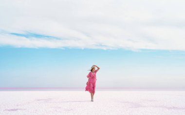 Güzel gökyüzü ve pembe göl üzerindeki tuzlu düzlüklerden oluşan güzel cennet manzarası. Pembe elbiseli romantik hayalperest kadın manzaranın tadını çıkarıyor.