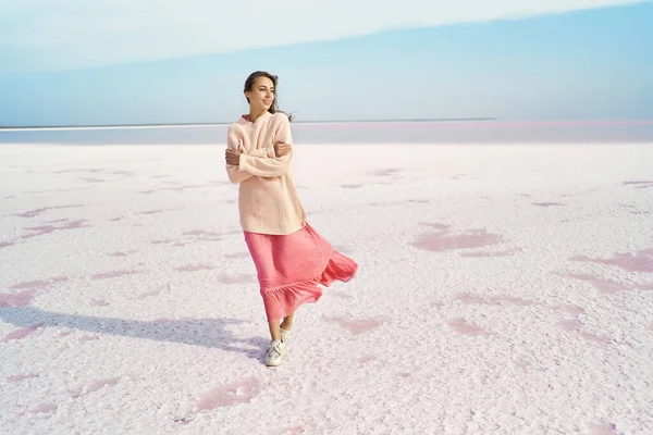 Maravilhosa mulher sonhadora em grande suéter e vestido rosa posando no litoral salgado ventoso no lago de sal rosa. imagem paraíso inspirado Imagens De Bancos De Imagens Sem Royalties