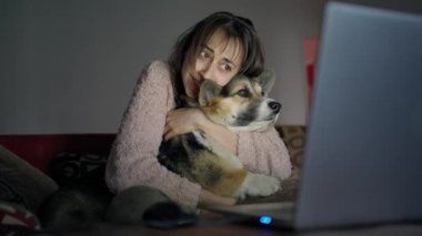 Sevecen bir kadın köpekle kanepede oturup film izler.