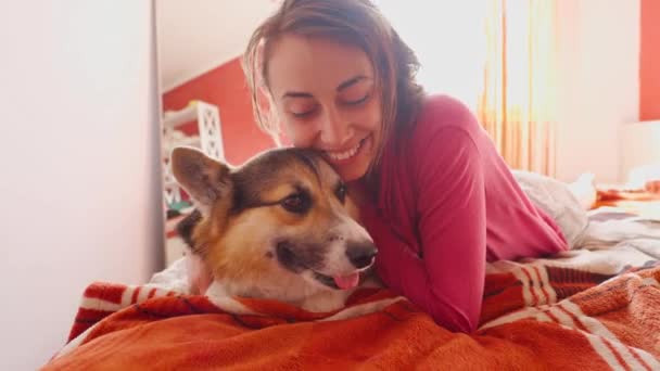 Милая молодая женщина гладит симпатичную собаку в постели — стоковое видео