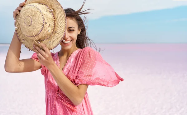 Mujer en vestido rosa en el paraíso paisaje de pisos de sal. chica sonriente cubriendo media cara con sombrero — Foto de Stock