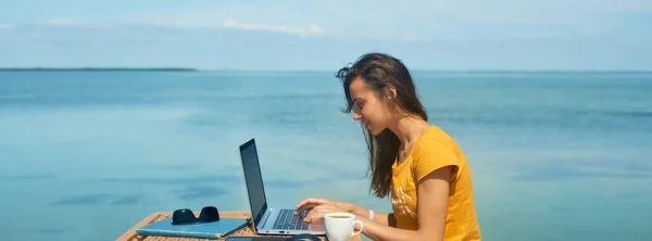 Panoraama kuva freelancer nainen työskentelee kannettavan tietokoneen ulkona sininen meri kaunis kesänäkymä — kuvapankkivalokuva