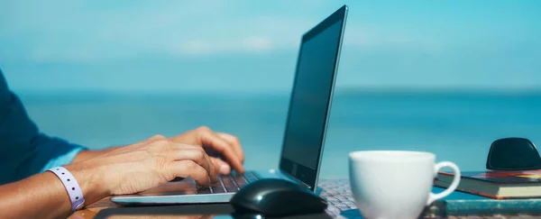 Panoraama kuva mies kädet kirjoittamalla tekstiä kannettavan tietokoneen edessä sininen meri ja kirkas taivas tekijänoikeusvapaita kuvapankkikuvia