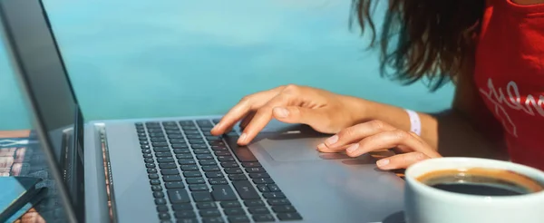 Panoramauttrykk kvinne hender skriver tekst på bærbar datamaskin med blå sjøbakgrunn stockbilde