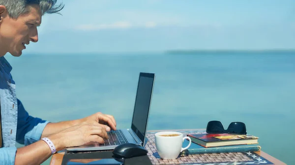 Panoramic image businessman working outdoors on laptop computer by beautiful blue sea view Stock Photo