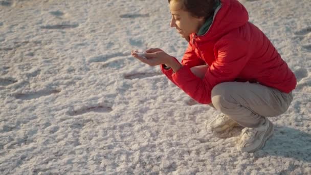 Woman in red jacket smiling and holding salt crystals in hands at beautiful landscape of Salt Flats — Stock Video