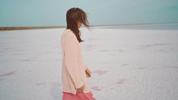 Caminante chica en suéter grande y soplado vestido rosa en el hermoso paisaje de pisos de sal en el lago rosa — Vídeos de Stock