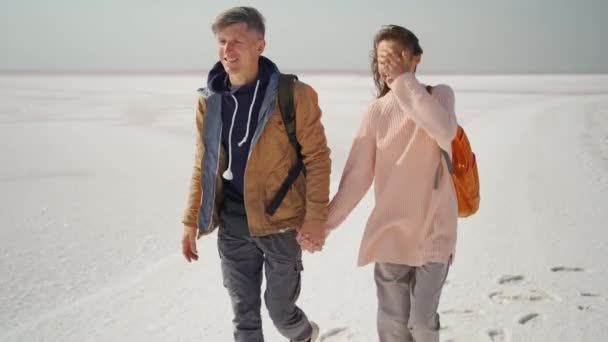Šťastný krásný pár cestovatelé chůze ruku v ruce na růžové bílé slané pobřeží — Stock video