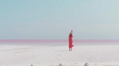 Güzel gökyüzü ve pembe göl üzerindeki tuzlu düzlüklerden oluşan güzel cennet manzarası. Pembe elbiseli romantik hayalperest kadın manzaranın tadını çıkarıyor.