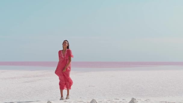Gelukkig zorgeloze elegante vrouw in blazende roze jurk geniet van haar vakantie tijdens het wandelen langs witte zoute strand met uitzicht op het paradijs — Stockvideo