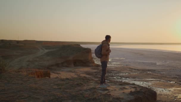 Sırt çantalı bir gezgin terk edilmiş deniz sahilinde gün doğumuyla buluşuyor. — Stok video