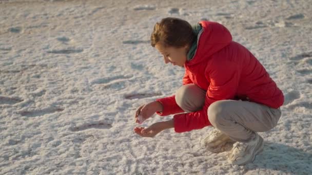 Mujer en chaqueta roja sonriendo y sosteniendo cristales de sal en las manos en el hermoso paisaje de Salt Flats — Vídeos de Stock